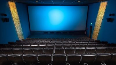 Sala de cinema vazia com poltronas e tela de projeção em ambiente escuro