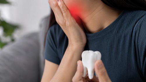 Mulher com dor de dente segurando a região da mandíbula, ilustrando problemas de saúde bucal.