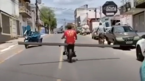 Motociclista transporta tronco de madeira em avenida de Jequié, na Bahia.