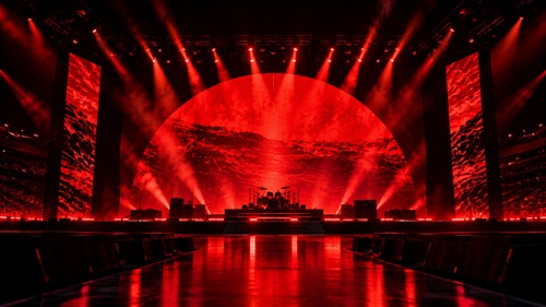 Palco de show com iluminação vermelha, instrumentos e estrutura de som, sem público ou músicos.