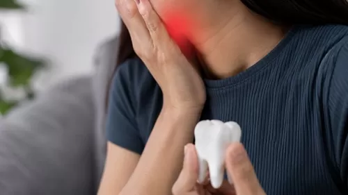 Mulher com dor de dente segurando a região da mandíbula, ilustrando problemas de saúde bucal.