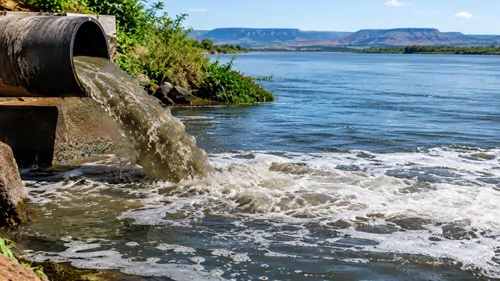 Tubulação despejando água escura e resíduos em um grande rio.