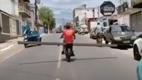 Motociclista transporta tronco de madeira em avenida de Jequié, na Bahia.