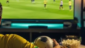 Pessoa assistindo partida de futebol pela televisão em casa